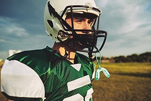 Teen with green sportsguard hanging from football helmet