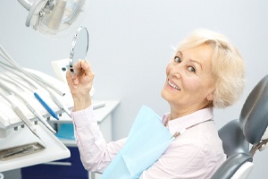 Happy patient admiring her new dentures in mirror