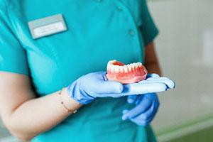 Full denture resting on gloved hand of dental team member 