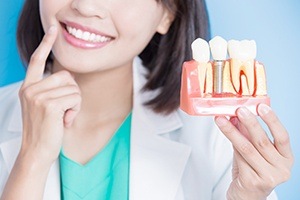 Dentist holding up model of dental implant replacement tooth and natural tooth