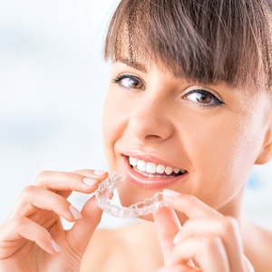 Smiling woman holding her aligner for Invisalign in Westborough