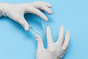 Gloved hands holding Invisalign® aligner against blue background