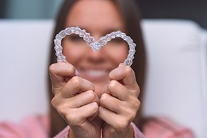 Woman holding two Invisalign aligners in heart shape