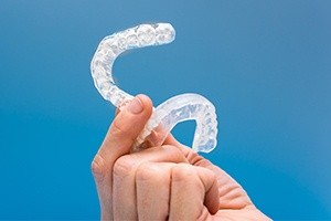 Hand holding up set of clear nightguards for bruxism