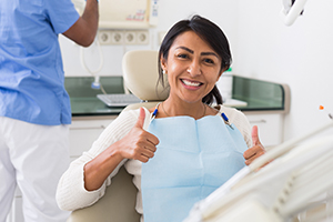 Woman in dental chair giving thumbs up during dental sedation visit