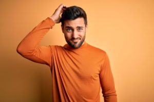 Curious man in orange shirt scratching his head