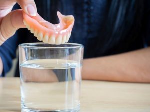 Hand placing denture in glass of water