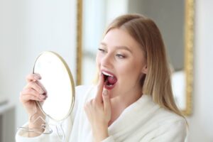 Woman in white robe, looking at her teeth in mirror