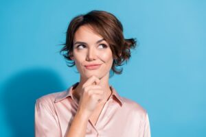 Woman standing against blue background, wearing curious expression